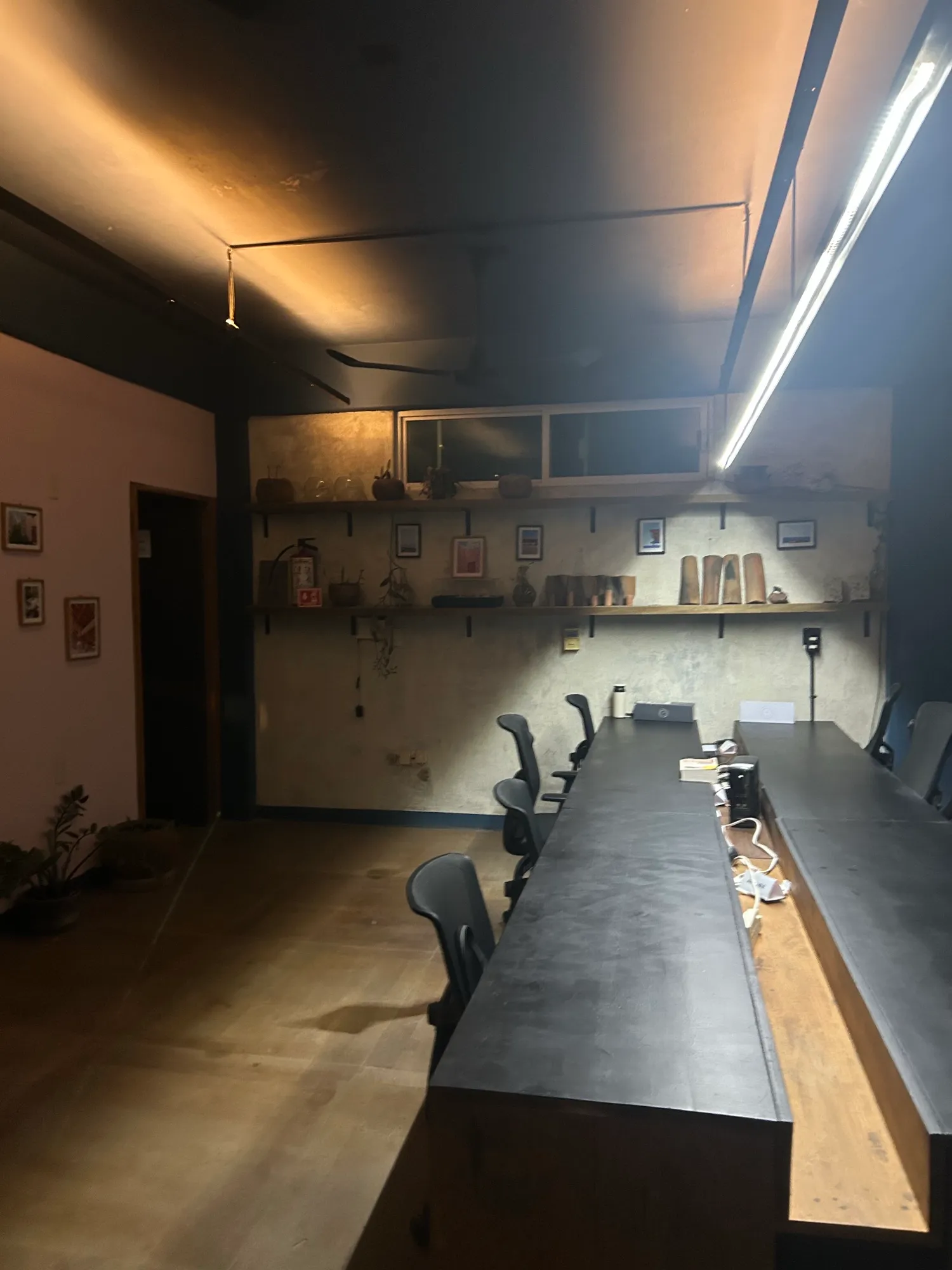 Mesa larga de trabajo con sillas y repisas en la pared al fondo