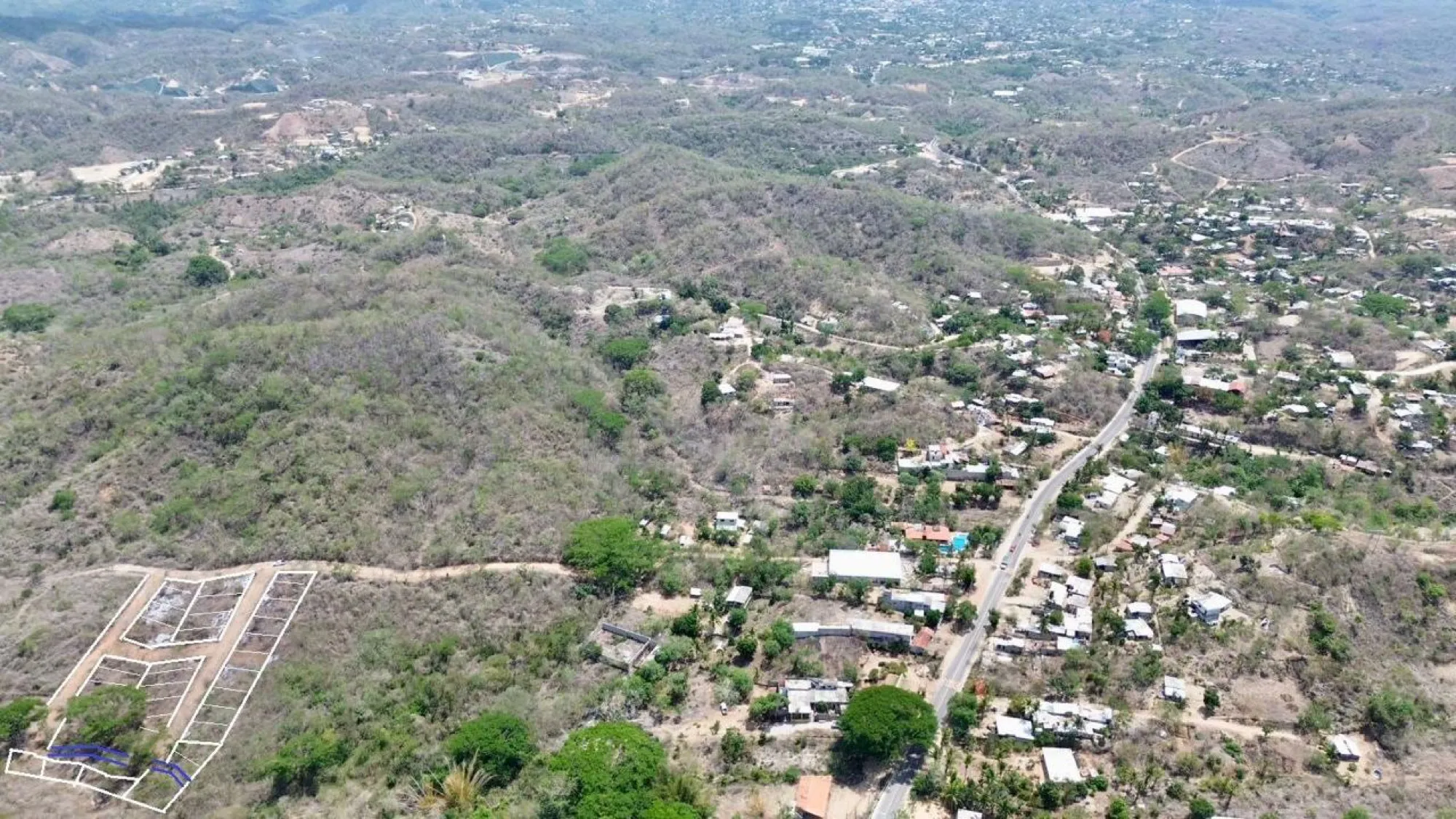 Vista aérea amplia de un poblado con casas y una calle, con un terreno trazado en la esquina