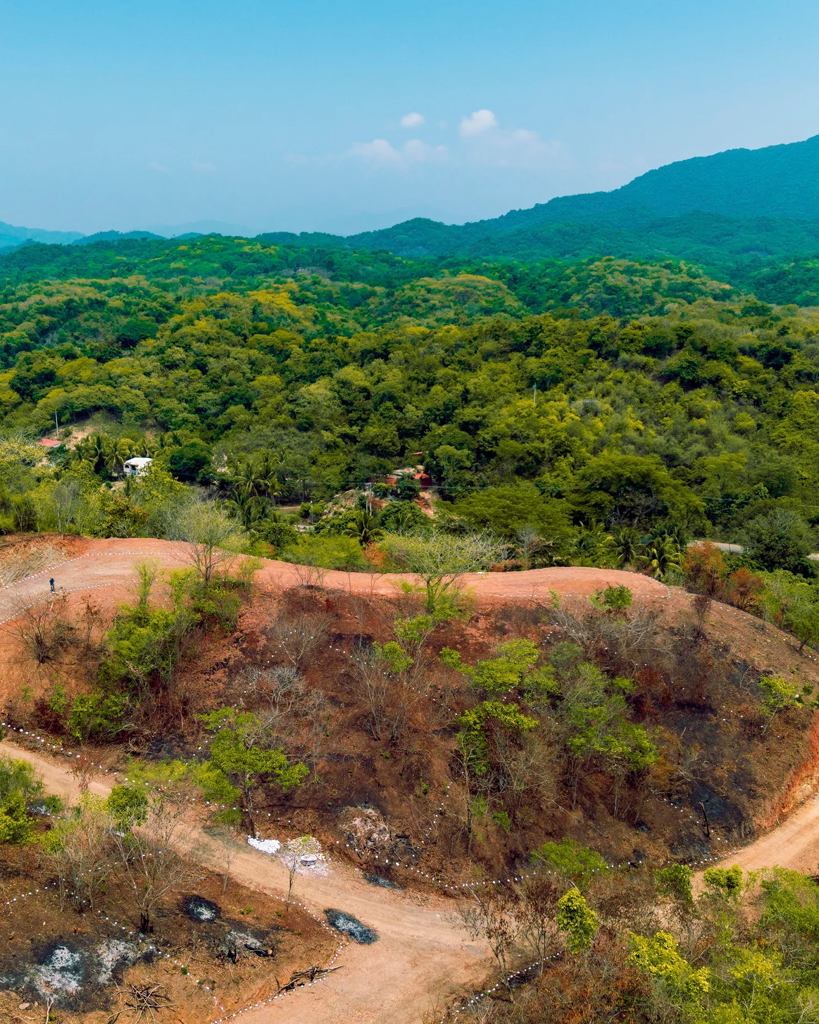 Ladera de tierra con vegetación y cerros al fondo